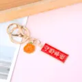 Macro view of inspirational gold metal keychain featuring an orange charm and red plaque - Rectangle Dreams Come True (Orange Charm)