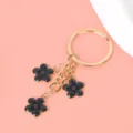 Gedetailleerde weergave van zwarte emaille kersenbloesem bedeltjes aan een gouden metalen hanger - Sleutelring Stijl / Zwart