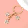 Detail van goudkleurige metalen sleutelhanger met drie witte kersenbloesem bedeltjes. - Sleutelring Stijl / Wit