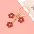Detailed view of a gold-tone metal keychain with three red enamel cherry blossom charms. - Red