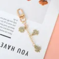 Close-up detail of a golden lucky three-leaf clover keychain with sparkling rhinestones. - Gold