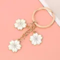 Detailed view of gold-toned metal keychain with white enamel cherry blossom petals. - White