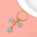Close-up of gold metal keychain featuring three light blue enamel cherry blossom charms - Key Ring Style / Sky Blue