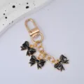 Close-up detail of black bow keychain accessory featuring three enamel charms - Black