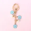 Detailed view of light blue sakura charms and white pearls on a gold-toned keychain - Plum Blossom / Blue