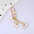 Detail view of gold keychain with three white enamel bow charms for bag decoration - White