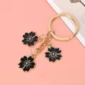 Detailed view of the black enamel cherry blossom charms on a gold-tone keychain. - Black