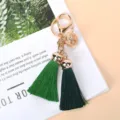 Vue détaillée d'un porte-clés doré avec une cloche et deux pompons verts élégants - Vert Foncé et Vert