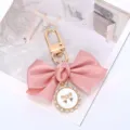 Close-up of the elegant pink satin bow keychain with a pearl-rimmed enamel charm - Pink