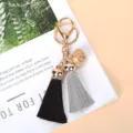 Vue détaillée d'un porte-clés avec cloche dorée et double gland sur magazine blanc - Gris + Noir