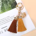 Close-up of golden hollow bell and double colored tassels on a stylish keychain charm - Brown And Orange
