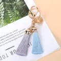 Detailed view of the gold hollow bell and dual-colored tassels on a stylish keychain. - Light Purple And Blue