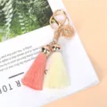 Detailed view of golden bell and soft tassels on a stylish pink and cream keychain pendant - Pink + Apricot