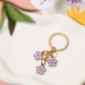 Detailed view of three purple enamel flower pendants on a gold-tone metal keychain - Purple