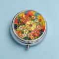 Macro view of a round silver pill box with a vibrant, colorful floral oil painting pattern - Blazing Gold Flower Cluster (Round Silver Frame)