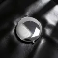 Close-up of a polished chrome folding makeup mirror on a textured black leather surface - Silver
