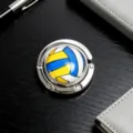 Faltbarer Taschenhaken aus Metall mit buntem Volleyballmuster auf einem dunklen Tisch. - Volleyball