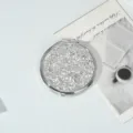 Overhead view of a round silver glitter compact mirror on white lifestyle background - Silver Style
