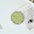 Detailed view of the sparkling lime green glitter on a round metal compact mirror. - Turquoise Green