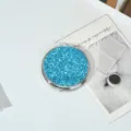 Close-up of portable metal makeup mirror with vibrant blue glitter surface finish. - Sparkle Blue
