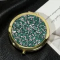 Detailed close-up of a portable round folding mirror with green glitter and silver studs - 70mm / Sapphire blue (gold frame)