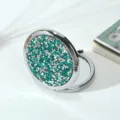 Detailed view of round metal folding makeup mirror with sparkling green rhinestones - 70mm / Sapphire blue (silver frame)