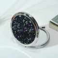 A detailed view of a round folding makeup mirror with a black diamond glitter lid. - 70mm / Obsidian color (silver frame)
