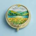 Round gold metal pill box featuring a 3D embossed colorful landscape lid illustration - Golden Mountain Flower Field (Round Gold Frame)