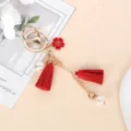 Detail of a cute red tassel keychain with flower charm and pearls for bag decor. - Red