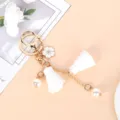 Close-up of elegant gold keychain with white cherry blossom, tassels and pearls - White