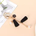 Macro detail of elegant gold keychain featuring black flower charm, tassels and white pearls - Black