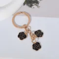 Detailed view of a boutique gold-plated keychain with three black enamel rose charms. - Black