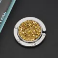 Macro-opname van een opvouwbare tassenhaak met fonkelende gouden strass-steentjes. - Gele Zirkonia