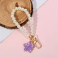 Close-up of pearl phone chain with purple flower charm and golden clasp on wood background - Purple 5-Petal Enamel Flower Style (Style 21)