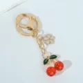 Elegant gold keychain featuring bright red resin cherries and a delicate cream flower charm - Red Transparent Cherry Sakura
