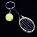 Detalle de un llavero con mini raqueta de tenis y pelota amarilla sobre fondo oscuro. - Verde Dorado Claro