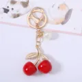 Detailed close-up of a sweet red cherry keychain with golden leaves and white pearl. - Red