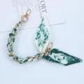 Macro view of woven green silk scarf and gold chain phone strap with metal lobster clasps - Style J