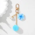Detailed macro view of blue resin flower and soft pom-pom keychain with gold chain - Blue