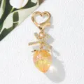 Close-up of a sweet yellow strawberry keychain with rhinestone bow and heart clasp charm - Transparent Orange
