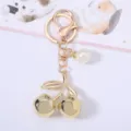 Detailed macro view of a golden cherry keychain featuring an elegant white pearl charm accessory. - Gold