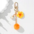 Close-up detail of yellow resin plumeria flower and orange fur pom-pom keychain charm. - Orange