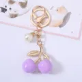 Detailed close-up of a purple cherry keychain with gold metal leaves and pearl charm - Purple