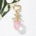 Detail view of a cute pink strawberry keychain with a crystal bow and heart-shaped clasp - Transparent Pink