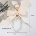 Detailed close-up showing a large beige bow and pearl bead loop keychain for bag accessory - White