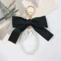 Detailed view of black bow and pearl loop keychain with gold female profile charm. - Black