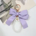Detail of an elegant purple satin bow keychain featuring a white pearl loop and gold charm - Purple