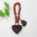 Detalle de un colgante de corazón de cuero marrón con cadena naranja para bolso de moda. - Marrón