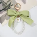 Close-up of green satin bow keychain featuring elegant pearl loop and gold-tone charm - Green