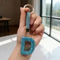 Close-up of a sparkling blue rhinestone letter D keychain with gold hardware held in hand. - Letter D